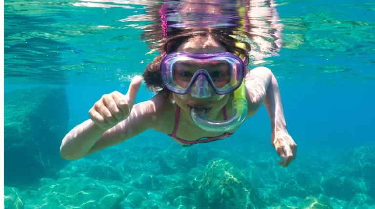 Enfant apprenant le snorkeling avec un instructeur dans une mer bleu clair